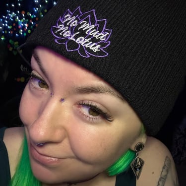 A smiling woman with green hair and a black beanie that says "no mud no lotus"