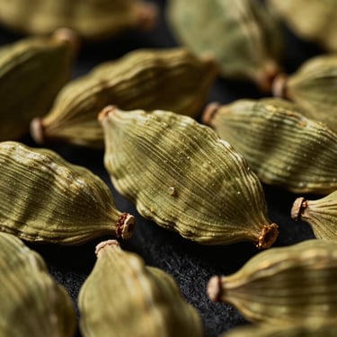 Moody macro close-up of green cardamom pods, dramatic side lighting, shallow depth of field, warm gold accents