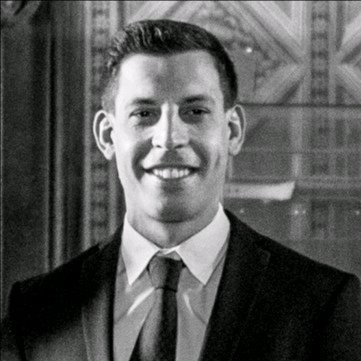 A black and white professional portrait of a smiling man in a suit and tie.