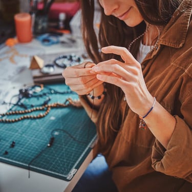 mujer elaborando joyeria con hilo de macrame y cuentas de piedras minerales en escritorio con mesa de corte