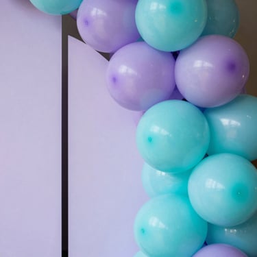 Close-up of a thematic children birthday balloon backdrop with pastel purple and bright turquoise balloons, clean geometric panels