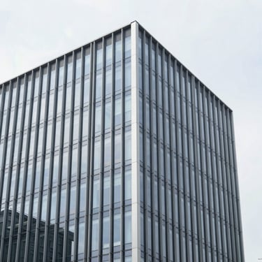 Straight-on elevation of a modern commercial office building facade, structural glazing reflecting a crisp overcast sky, clean vertical lines, desaturated cool tones