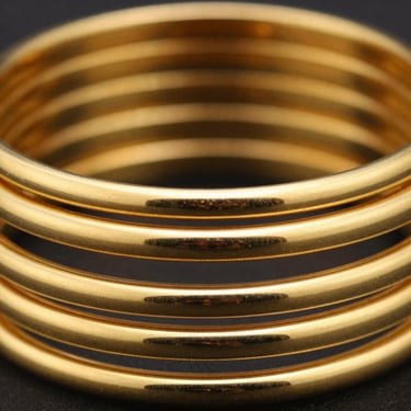 A stack of thick, hand-carved gold bangles with matte and polished finishes, close-up shot, shallow depth of field, luxury feel.