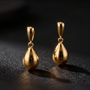 Close-up studio shot of elegant gold drop earrings, dramatic high-contrast lighting, soft golden glow, dark minimalist background.
