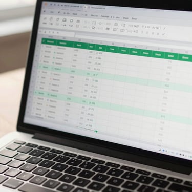 Overhead wide shot of a modern laptop screen displaying a clean Excel dashboard with green-tinted data cells, formula bar visible, soft natural light from the left, keyboard partially in frame, slight lens warmth