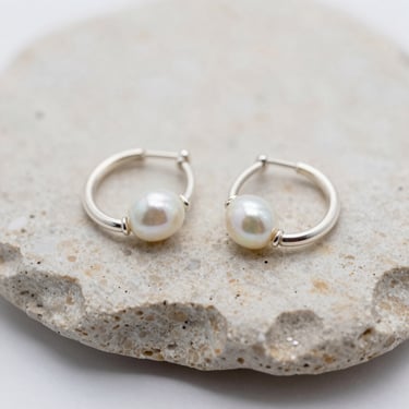 Macro shot of silver hoop earrings resting on a piece of raw travertine stone, soft diffused daylight.