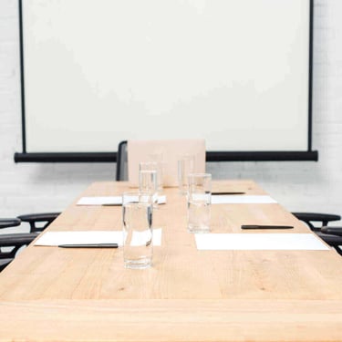 Empty corporate meeting room with water glasses, pens, and paper on a wooden table before a presentation.