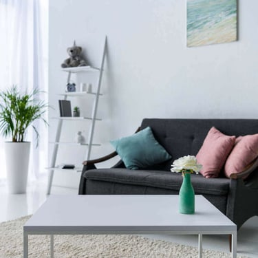 Modern living room with a white coffee table, grey sofa, and leaning ladder bookshelf decor.