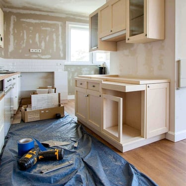 Professional kitchen renovation featuring new wood cabinets, power tools, and white subway tile backsplash installation.