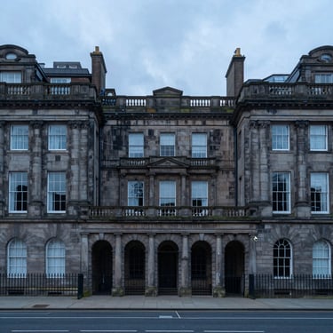 Straight-on architectural shot of historic stone buildings, overcast daylight, clean geometric composition