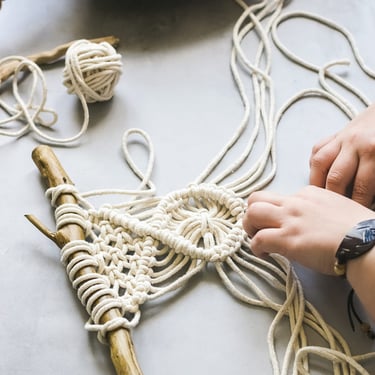 Manos sobre mesa realizando bordado de macramé con un palo de madera como base