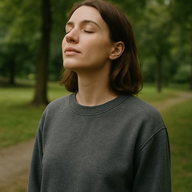 A person in comfortable clothes taking a deep, relaxed breath outdoors in a quiet, green park in Poland, soft focus background.