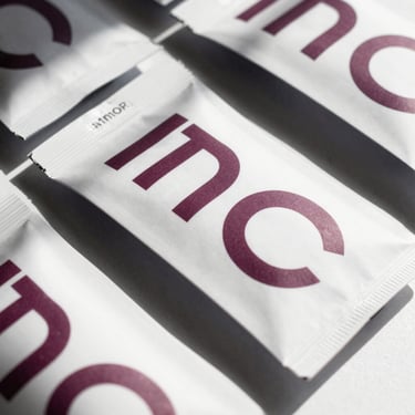 Close-up of physical brand collateral, sleek modern packaging with deep mauve typography on pure white paper, sharp high-contrast lighting, dramatic shadows
