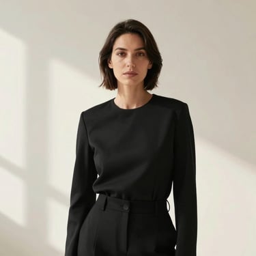 A professional portrait of a female creative director in a minimalist black outfit, standing against a soft off-white background, lit with soft natural light.