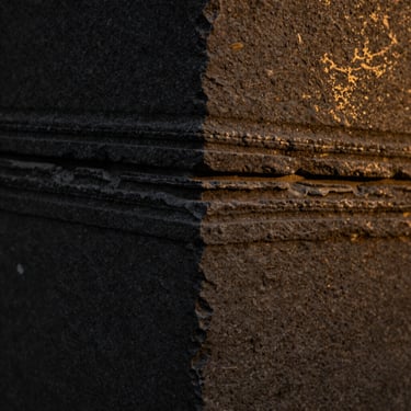 Macro close-up of cleft-finish Kota stone, low-key side lighting showing fine geological layers and matte charcoal surface, 35mm.