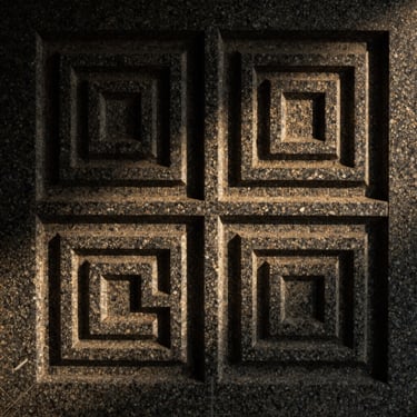 Bespoke carved stone relief panel, precise geometric architectural details cut into dark granite, low-key side-lit studio shot, 35mm.