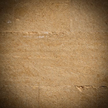 Close-up of hand-dressed Indian sandstone, fine-grained warm beige texture with subtle geological banding under dramatic side lighting, 35mm.
