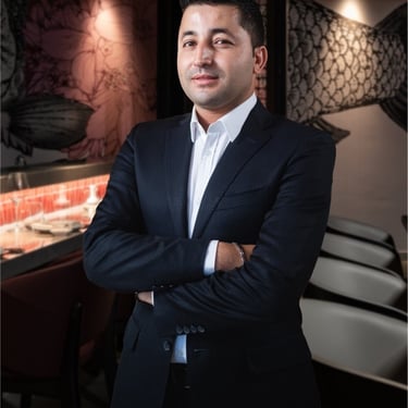 Professional male entrepreneur in a navy suit posing in a modern restaurant setting.