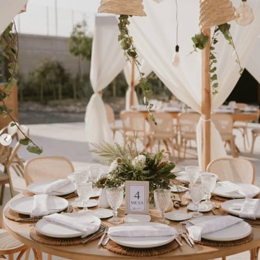 Mesa redonda decorada con vajilla blanca y detalles en madera.