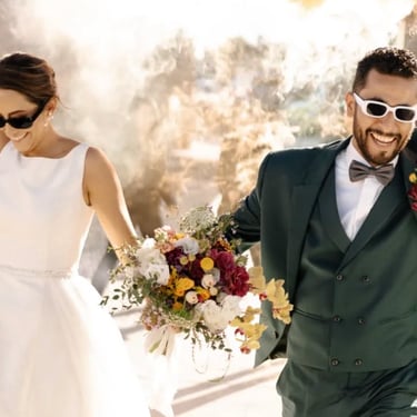 Pareja recién casada caminando con ramo colorido en exterior.