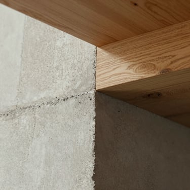 Close-up detail of honest materials, raw concrete texture meeting a warm wooden beam, soft natural lighting, architectural vignette