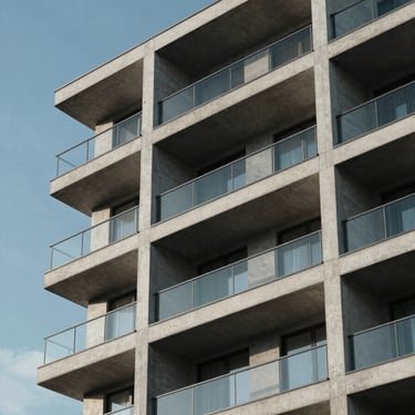 Architectural detail of a contemporary glass and concrete residential building against a clear blue sky.