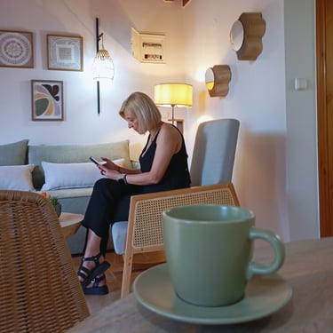 A woman checking her phone while enjoying a cup of coffee at Tonia's Cottage