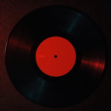 Cinematic 35mm photograph of a vinyl record cover, high-contrast black and red artwork, abstract minimalist design, heavy film grain.