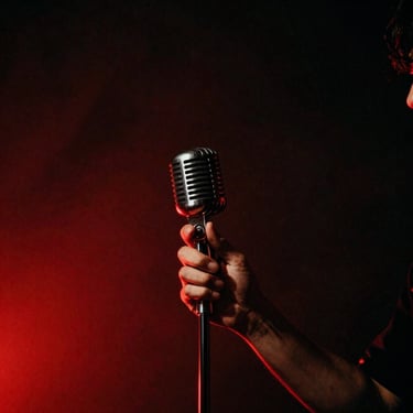 Cinematic film photograph of a singer's hands holding a vintage microphone, dark background with deep red shadows, smoky atmosphere.