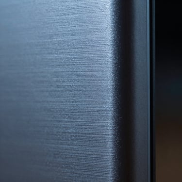 Extreme macro close-up of brushed metal consumer tech, cold blue edge lighting, high-contrast chiaroscuro, square crop.