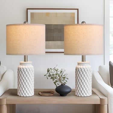 Pair of white textured ceramic table lamps with tan linen shades on a wooden console table.