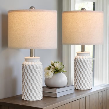 Pair of white ceramic table lamps with a textured honeycomb base and linen shades on a wooden sideboard.
