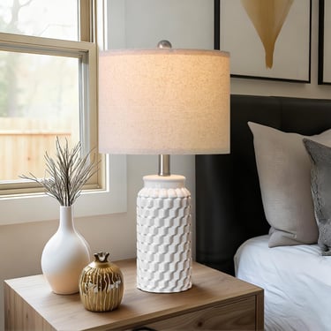 Modern white ceramic bedside table lamp with textured honeycomb base on a wooden nightstand.