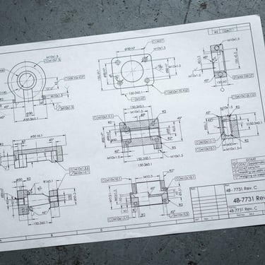 A crisp macro photograph of a technical spec sheet lying on a clean slate-gray factory workbench, cool natural daylight, sharp focus on engineering schematics.