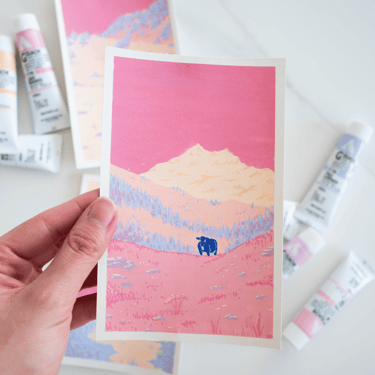 Fotografia de una manos sujetando una ilustración en gouache de un paisaje de montaña en tonos rosa y crema con una vaca azul