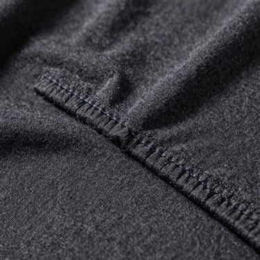 Extreme close-up of a flatlock stitch seam on a heavy charcoal cotton t-shirt, industrial daylight.