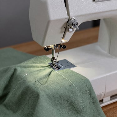 Close-up of a heavy-duty sewing machine sewing a clean french seam on sage green linen