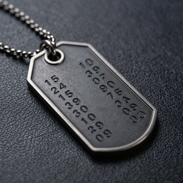 Macro shot of a black steel military tag with deep-etched coordinates, lying on textured dark leather, dramatic studio lighting