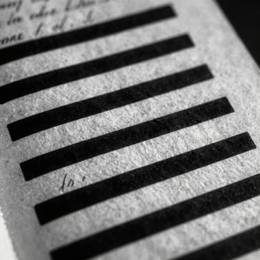 Extreme close-up of a weathered, handwritten historical document with parts redacted in heavy black ink, high contrast black and white, dramatic side lighting.
