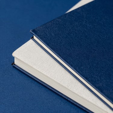 Close-up of a linen-bound notebook with textured paper edges on a deep cobalt background, dynamic angle, sharp focus