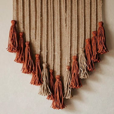 Earthy jute fiber wall hanging with layered textured tassels, warm terracotta accents