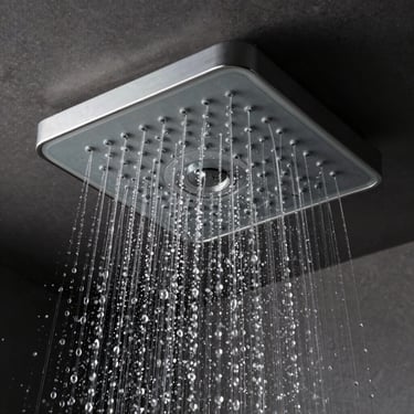 Macro shot of a monolithic square ceiling-mounted rain shower head, water droplets suspended in mid-air, dark background.