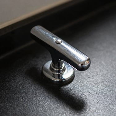 Macro detail of a chrome basin mixer handle, sharp shadows, dark obsidian background.