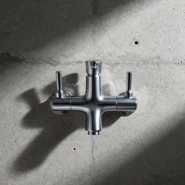 Symmetrical front view of a chrome basin mixer mounted on a raw concrete wall, dramatic side-lighting, sharp shadows.