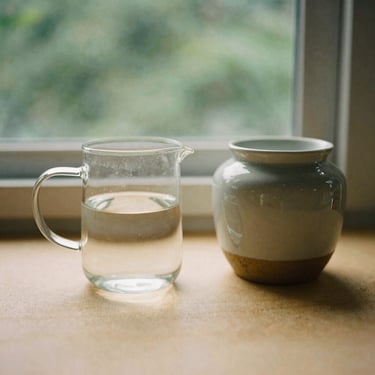 A glass pitcher of filtered water next to organic local coffee in a ceramic jar, warm sand tones, soft morning light