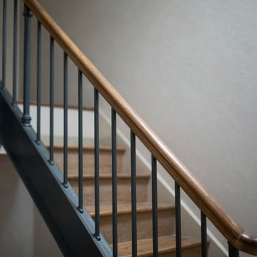 Tight architectural detail of a staircase handrail in an urban apartment building, overcast natural light, warm wood and painted metal, no people, precise and still