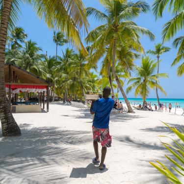Tourist carrying drinks on Saona Island beach with palm trees and turquoise water