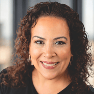 Professional headshot of a smiling woman with curly brown hair and gold hoop earrings.