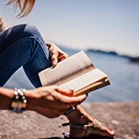 A woman sitting by the edge of a lake reading a book