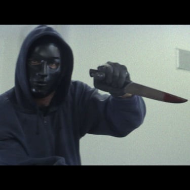 A man in a hooded sweater and black mask brandishes a long kitchen knife covered in blood
